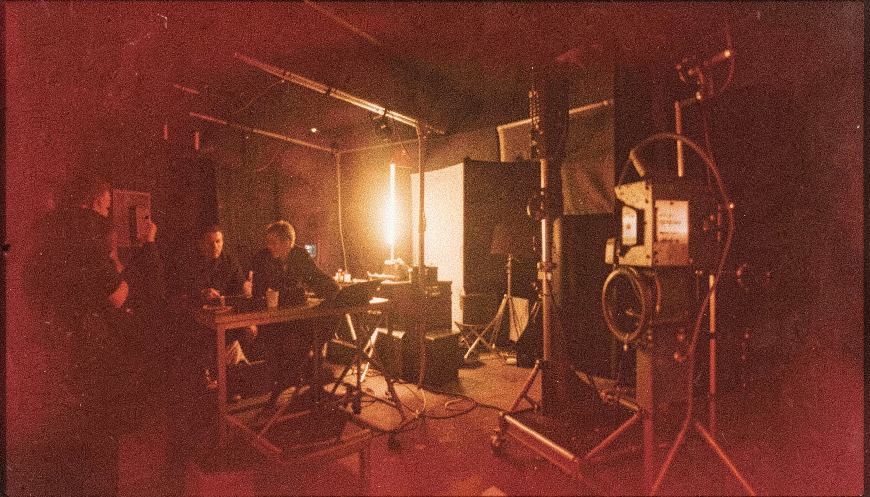 Analog film photograph with grain, depicting a film production setup with warm tungsten light, deep shadows, and rich amber tones